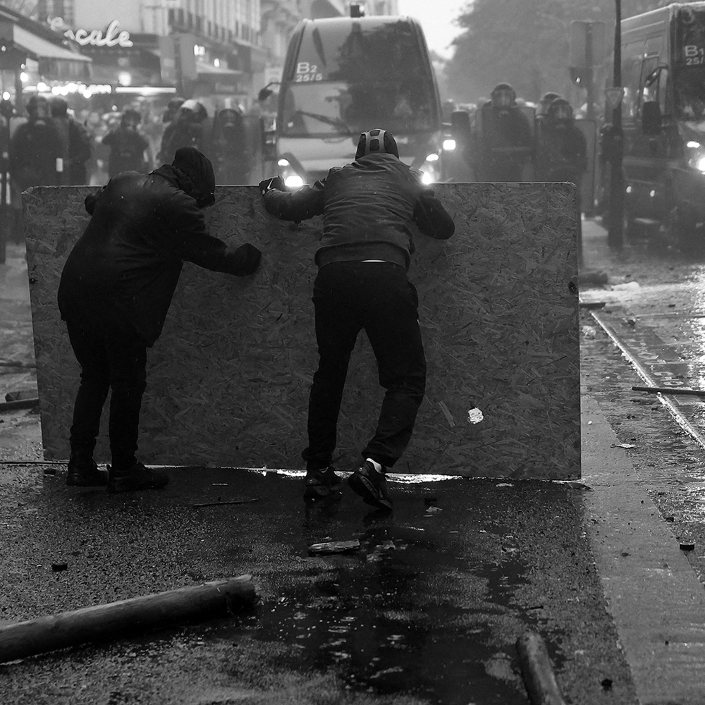 Protesters take cover behind a plywood board as they clash with French gendarmes during demonstrations in Paris, France, October 2026.
