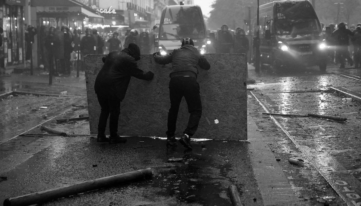 Protesters take cover behind a plywood board as they clash with French gendarmes during demonstrations in Paris, France, October 2026.